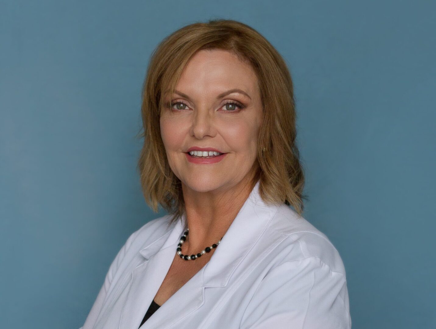 A woman in white jacket standing next to blue wall.